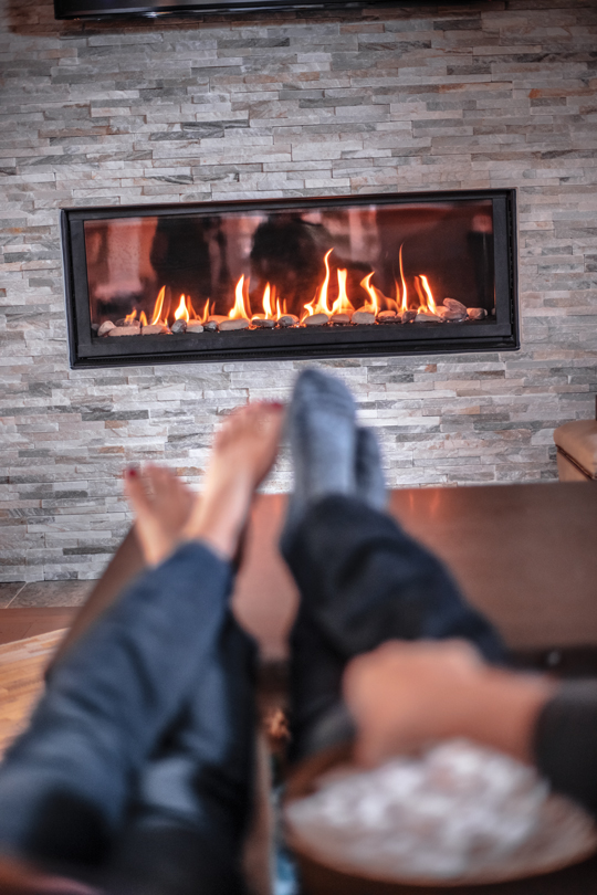 Couple sitting on a couch in their living room eating popcorn sitting next to propane fireplace. 