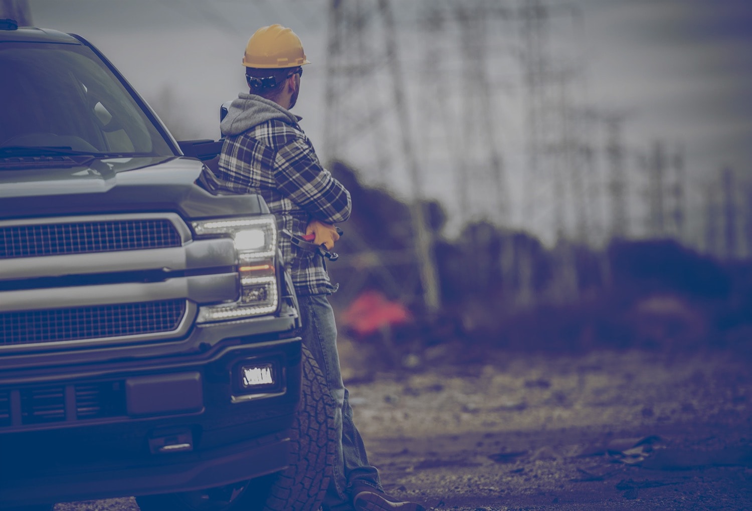Construction worker standing beside a pickup truck holding a hammer and looking at power lines. 