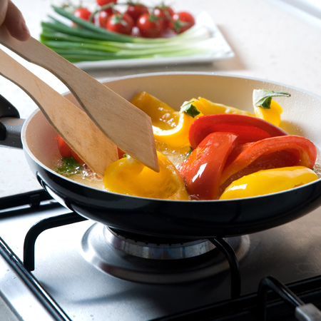 Cooking red and yellow bell peppers in a pan on a propane range element.