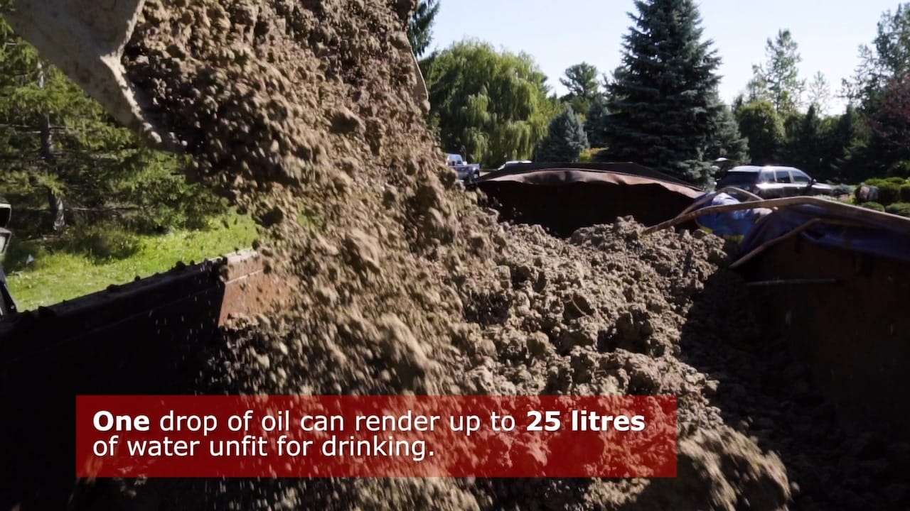 Screenshot from the Real Price of Oil video of dirt being dumped with on screen text: One drop of oil can render up to 25 litres of water unfit for drinking.