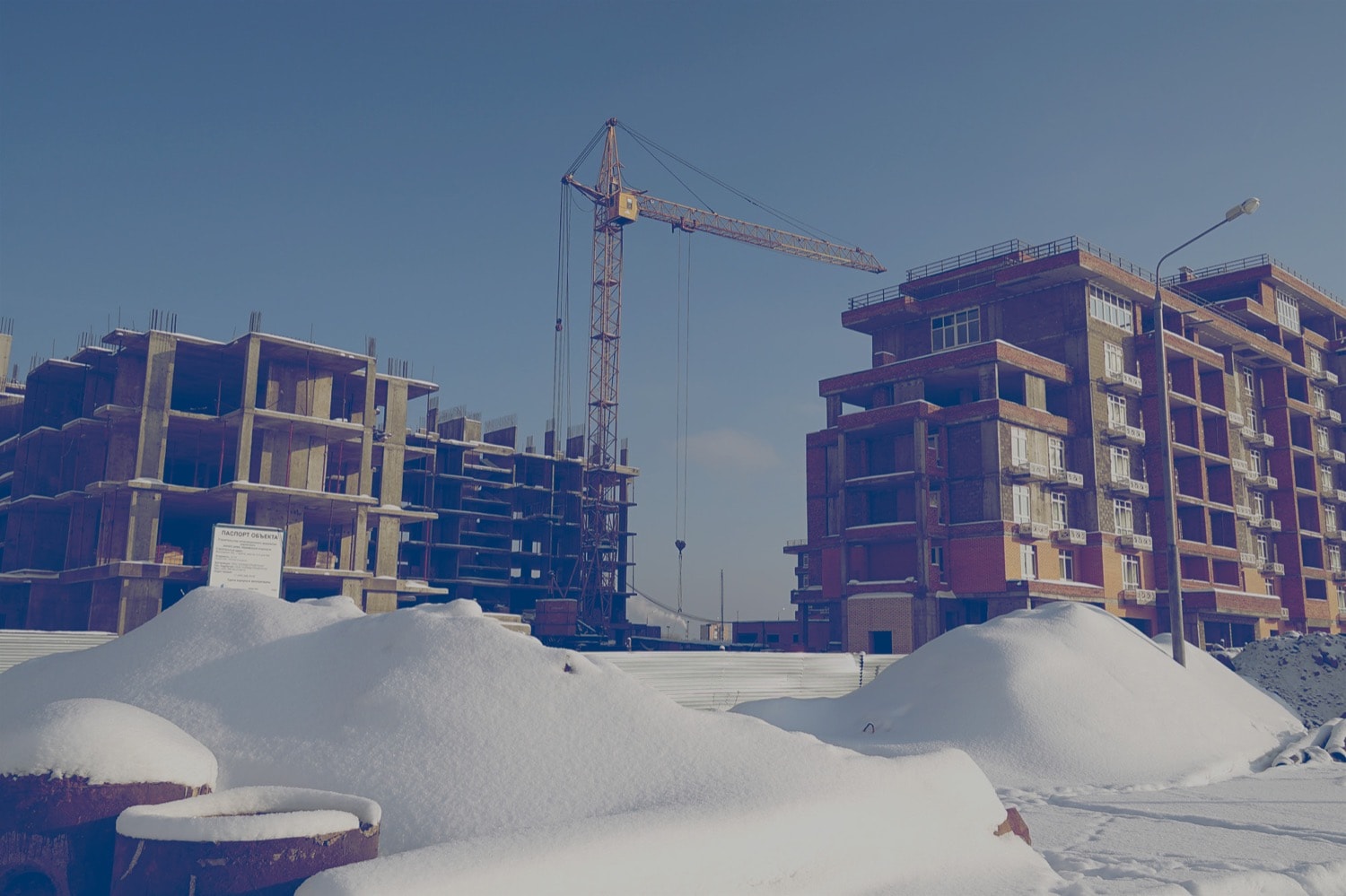 Two condos under construction with a crane in the background and snow on the ground. 