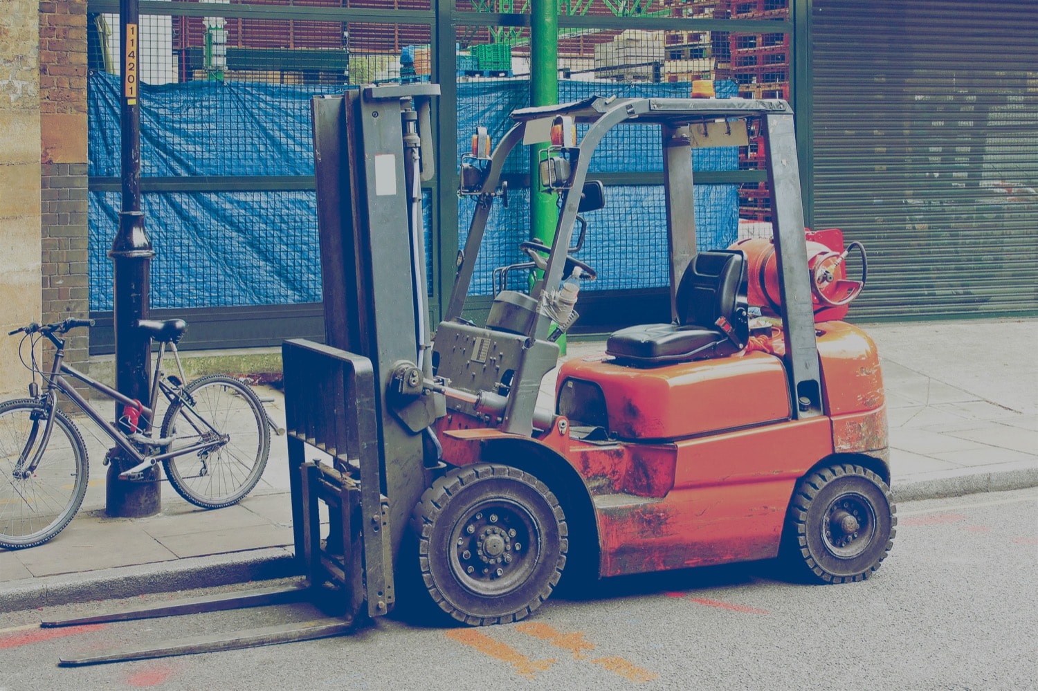 Orange forklift with propane cylinder parked on the street next to a bike. 