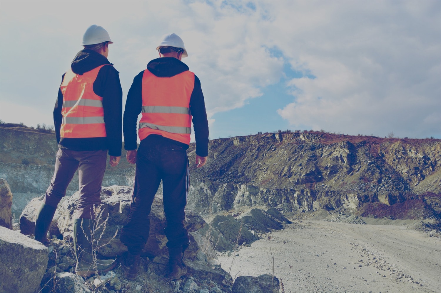 Two construction workers look at an expansive open-pit mine. 
