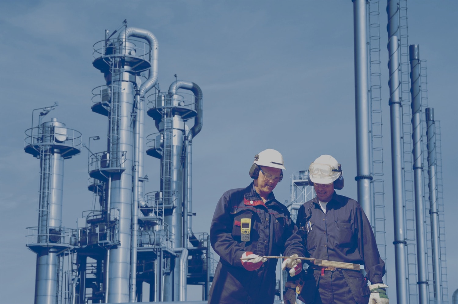Two workers in an oil field with a refinery in the background. 