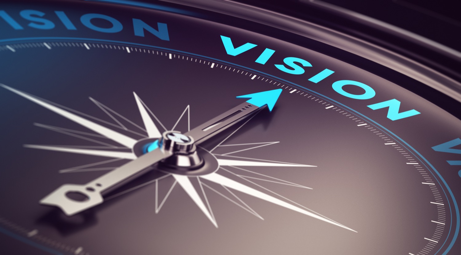 Closeup of a compass pointing to the word vision. 