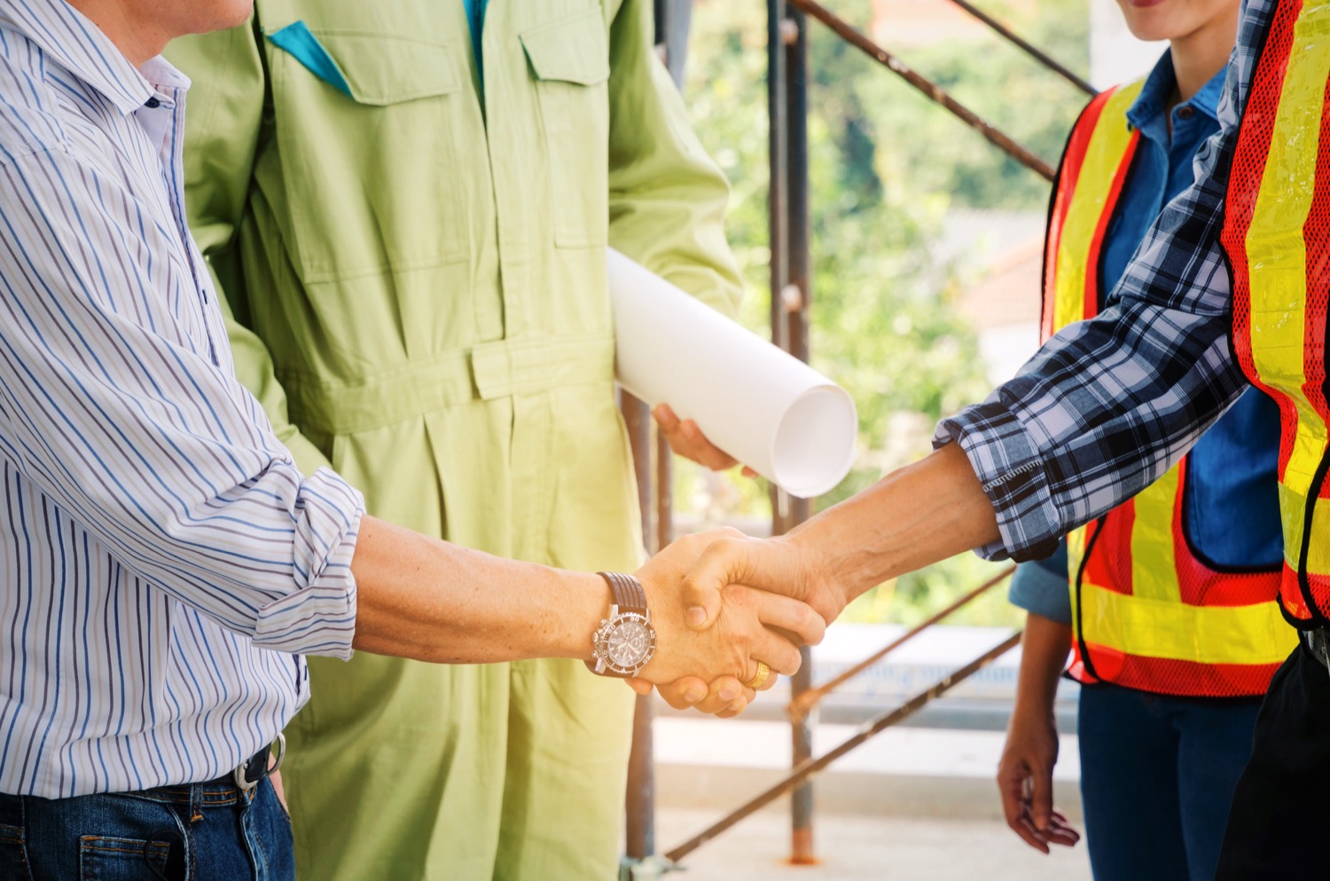 A close up of a contractor shaking hands with a man while another contractor and an architect stand beside them. 