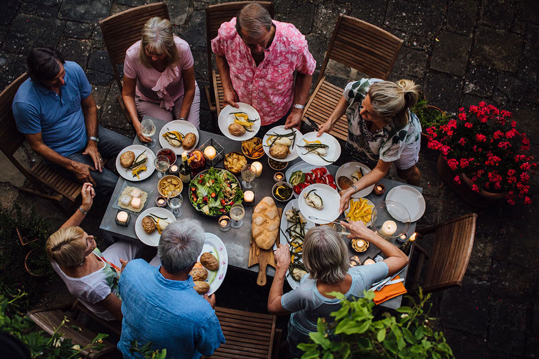 An overhead look at a group of adults sharing a large meal on an exterior patio that is heated by propane. 