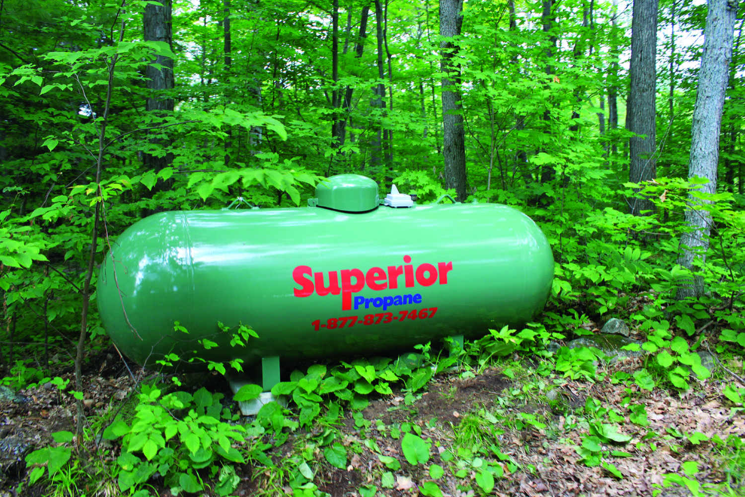 Green Superior Propane tank in a rural, forested area. SMART Tank sensor installed on top of the tank.