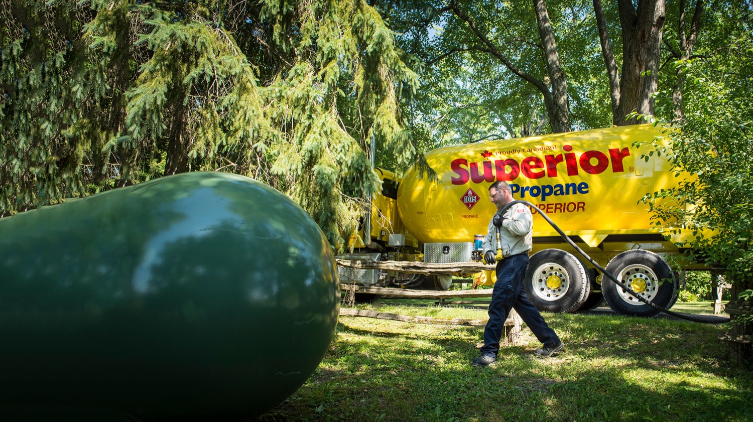 Superior Propane employee preparing to refill a green propane tank in a forested area. 