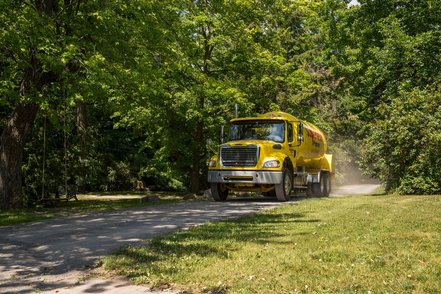 Superior Propane truck making a delivery to a home on a tree-lined rural dirt road. 