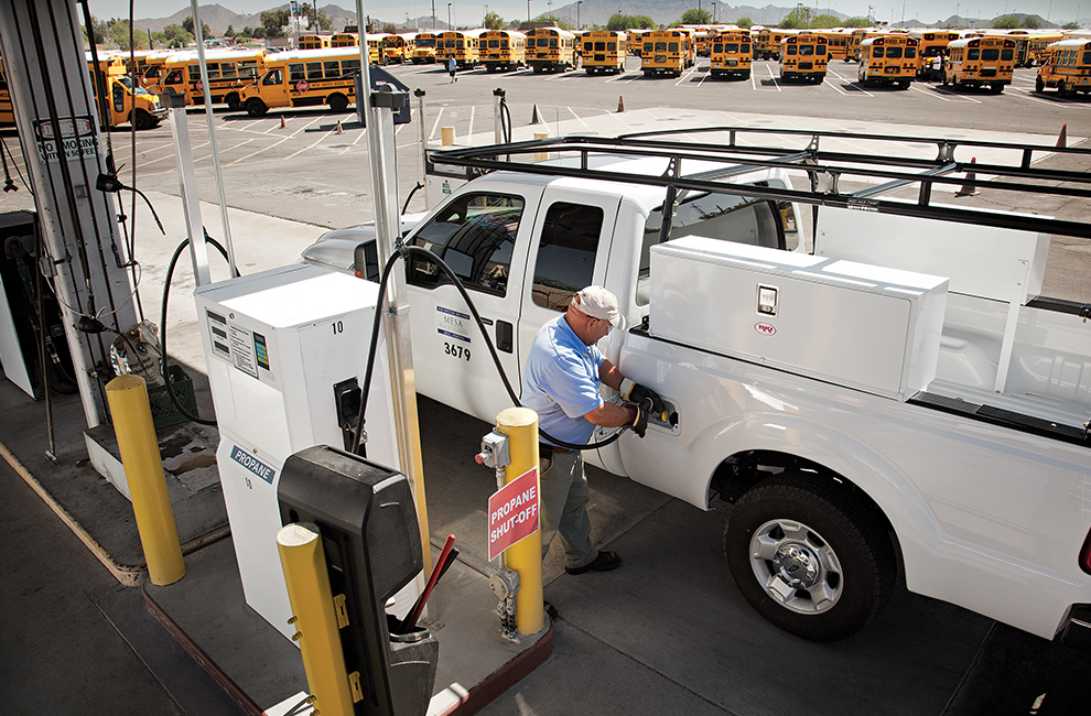 Man filling a pickup truck with propane autogas at a card lock station. There is a fleet of school buses in the background.
